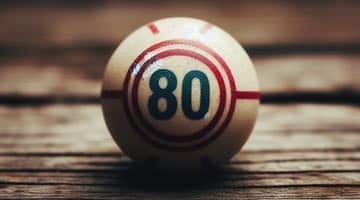 En bild på en bingoboll med nummer 80 som ligger på ett träbord.