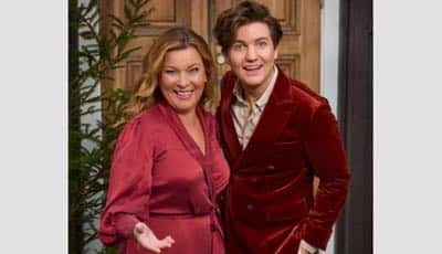 Uppesittarkvällens programledare Daniel Norberg och Lotta Engberg bredvid en gran. Bägge bär julröd klädsel.