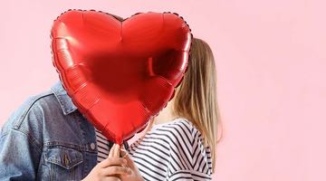 Kampanjbild för Miljonlotteriets bonuserbjudande för att fira Alla hjärtans dag. I bilden syns ett par som pussas bakom en röd hjärtformad ballong.